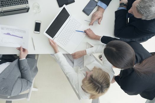 Business people brainstorming at office desk, analyzing financial reports and working with laptops and tablets