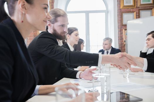 Business people sitting at the table in a row and work with documents, shaking hands