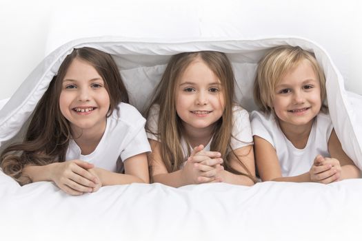 Three happy smiling children under blanket at home