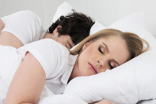 Young couple sleeping in bed with white blanket and pillows