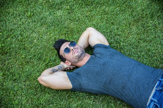 Good looking, fit male model relaxing lying on the grass, looking at camera, photographed right from above
