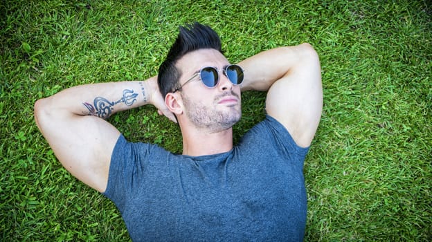 Good looking, fit male model relaxing lying on the grass, looking at camera, photographed right from above