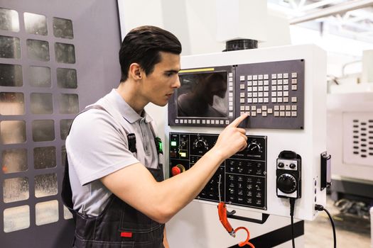 Worker pressing programming buttons on CNC machine control board in factory