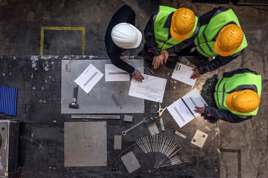 Workers and manager in safety helmets working with documents at factory