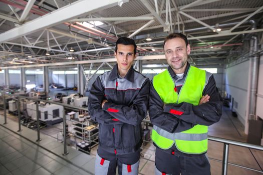 Team of two workers in uniform standing at background of CNC factory