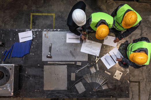 Workers and manager in safety helmets working with documents at factory