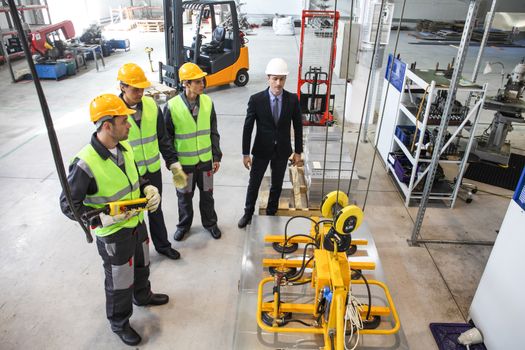Manager and workers near metal sheet lifting device at factory