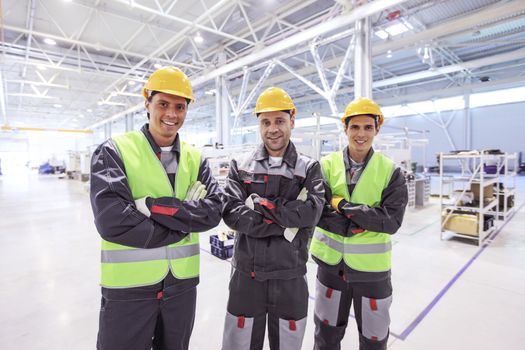 Team of three workers in uniform standing at background of CNC factory