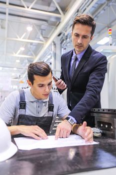 Manager and worker working with documents at plant near CNC machines