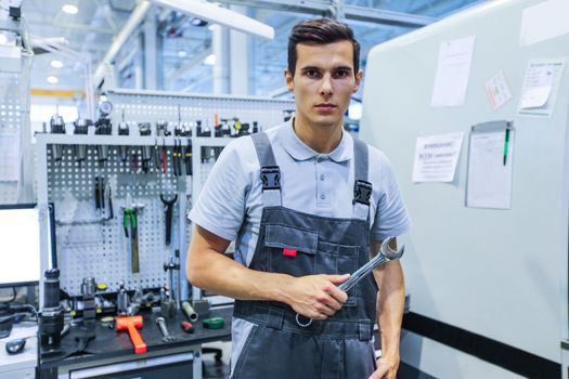 Portrait of a young worker holding wrench at workplace with computer and tools at CNC factory