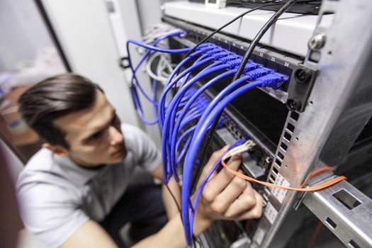 Young engeneer man in network server room connecting wires and checking rack devices