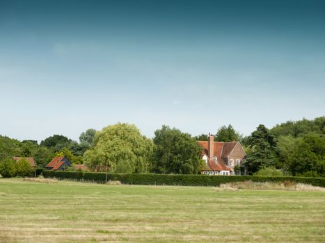 country farm house behind trees and field; Essex; UK