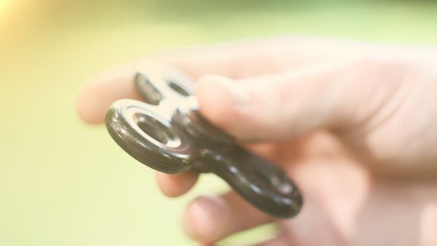 Playing with the black Fidget Spinner. Toy spinner in hand. Sun effect.