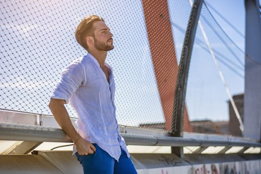 One handsome young man in urban setting in European city, standing against metal grid