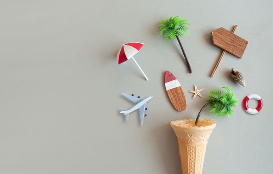 Icecream cone with various summer items including parasol, surfboard, miniature airplane and pine trees 