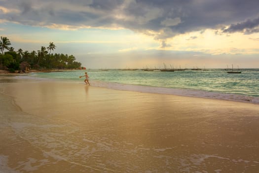 A nice beach with Several fishing boats  anchored at sunset with sunbeams and one woman running on the beach.Zanzibar coast,Tanzania.