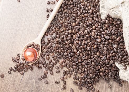 Coffee capsule on wooden spoon and  roasted coffee beans with burlap sack on wooden background,top view.