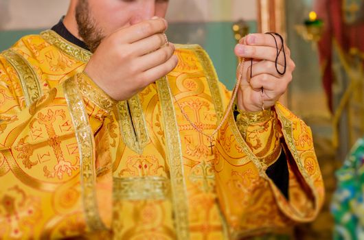 Priest hands holding golden chain with cross during christening