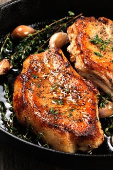 Juicy, browned pork steak on a bone in oil with garlic and herbs in a frying pan. 