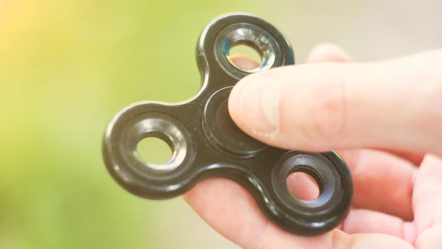 Playing with the black Fidget Spinner. Toy spinner in hand. Sun effect.