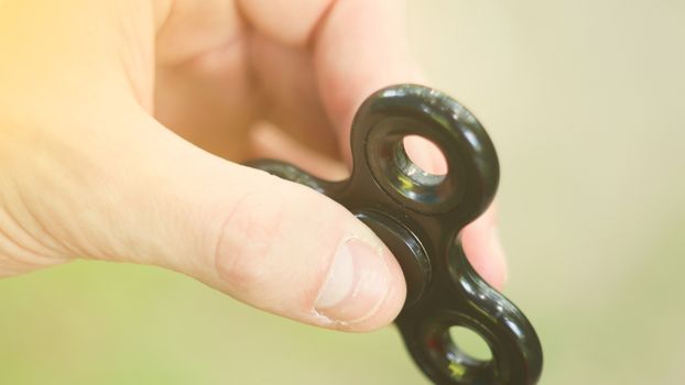 Playing with the black Fidget Spinner. Toy spinner in hand. Sun effect.