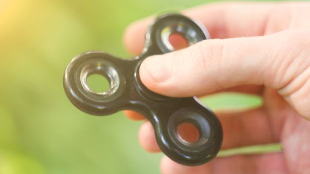 Playing with the black Fidget Spinner. Toy spinner in hand. Sun effect.