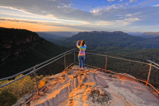 A female captures a stunning sunrise over mountainous landscape with her mobile phone