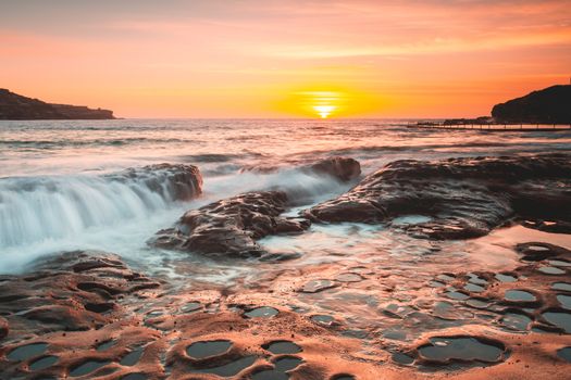 Summer sunrise light up the sky in warm tones and cast its beautiful light over the sea coast.  Australia