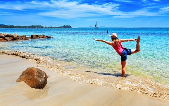 Balancing on moving sand.  A woman practices yoga on the beach with the shifting sands and tidal flows adding an extra dimension and difficulty to the usual asanas.