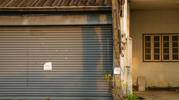 Dirty Vintage Roller Shutter Door with Blank Paper Note - Old Abandoned House for Sale  in Bangkok Thailand. Sunny Warm Day