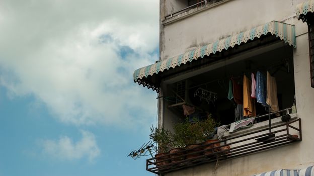 Vintage Blue Balcony Window with Colorful Clothes and Plant Pots on Rusty Metal Rack - Old Apartment. Bangkok Thailand.