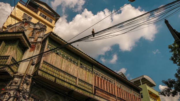 Ancient Wooden House with a Bird on Electric Wires. Low Angle View. Bright Sunny Sky with Clouds.