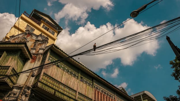 Ancient Wooden House with a Bird on Electric Wires. Low Angle View. Bright Sunny Sky with Clouds.