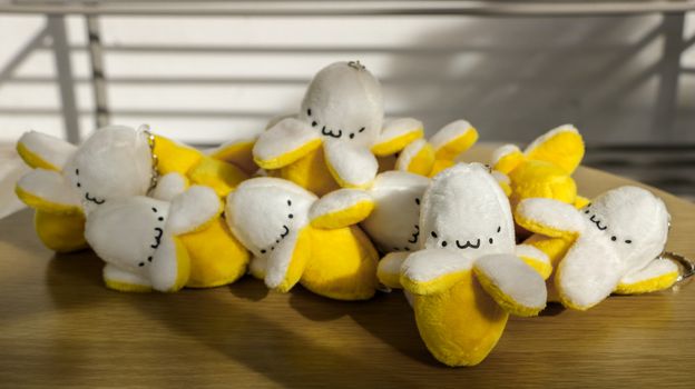 Miniature Stuffed Bananas/ Keychain/ Soft Toys with Cute Faces on Wooden Table in the Sun - Outdoors