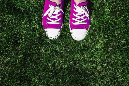 Legs in old pink sneakers on green grass. View from above. The concept of youth, spring and freedom.