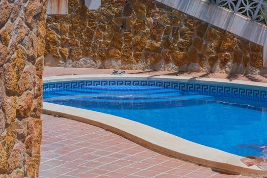 Luxury swimming pool with beautiful landscaping of the territory. In the background a mediterranean wall decorated with sandstones.
