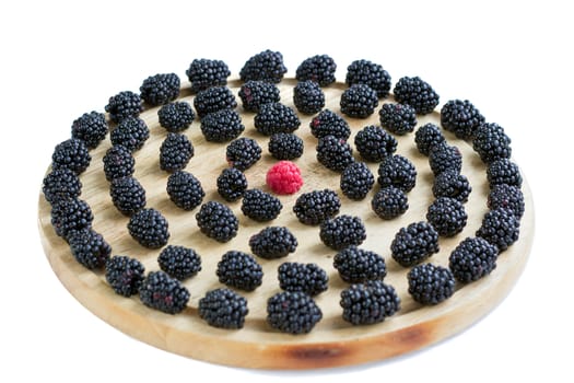 Tasty juicy berries set of many blackberries and one raspberry among them on light round wooden tray isolated