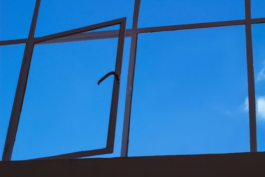 Blue sky view through big loft upper window with transparent glass cells and open leaf