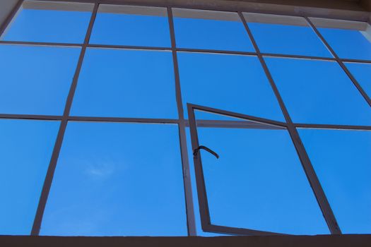 Blue sky view through big loft upper window with transparent glass cells and open leaf