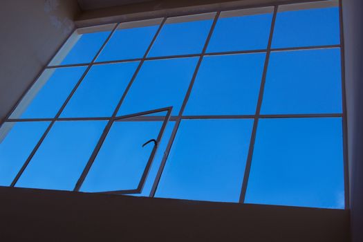 Blue sky view through big loft upper window with transparent glass cells and open leaf