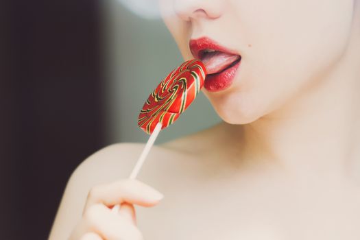 Crop side view of faceless slender woman licking twisted orange lollipop