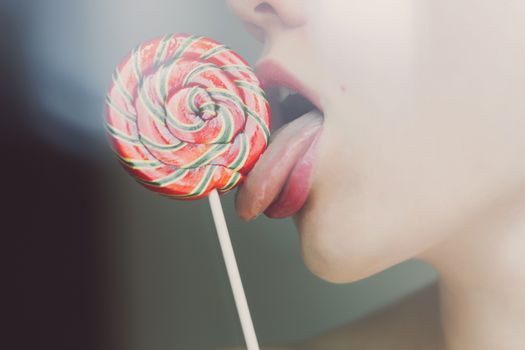 Crop side view of faceless slender woman licking twisted orange lollipop