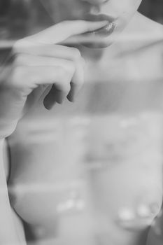 Crop view through glass of faceless naked young woman sexually putting finger in mouth