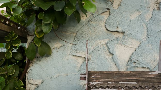 Wooden Roof Pattern with Peeling White Paint on Rough Painted Teal Wall - Green Leaves from the Garden - Miniature Wood Temple/ Spirit House in front of Local Home. Rural Thailand.