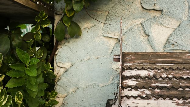 Wooden Roof Pattern with Peeling White Paint on Rough Painted Teal Wall - Green Leaves from the Garden - Miniature Wood Temple/ Spirit House in front of Local Home. Rural Thailand.