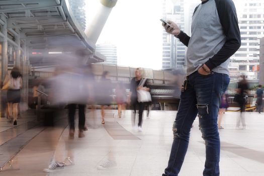 Man holding the phone with Motion Blurred People walking past