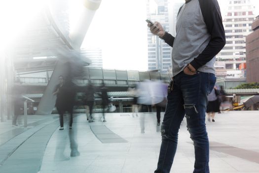 Man holding the phone with Motion Blurred People walking past