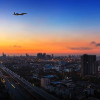 Silhouette of airplane flying in a sunset sky over the city at sunrise