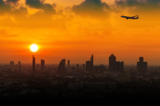 Silhouette of airplane flying in a sky over the city at sunset