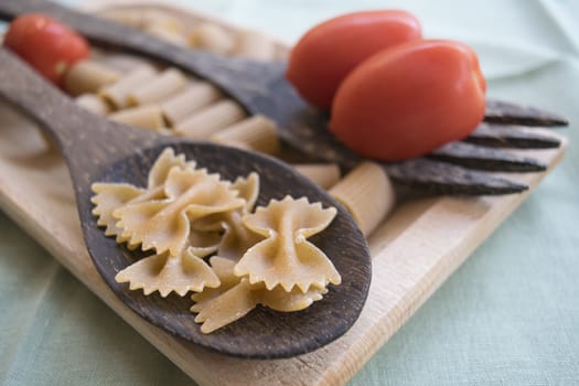 wholemeal butterfly pasta on a wooden ladle and fresh cherry tomatoes